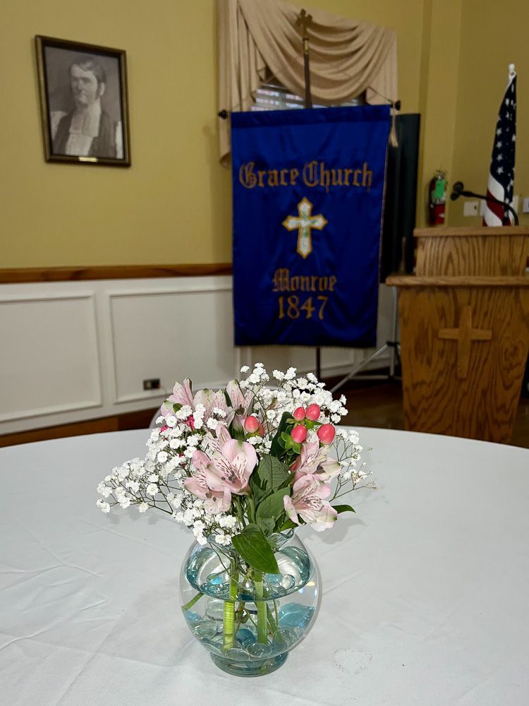 A vase of flowers sits on a table in front of a grace church banner
