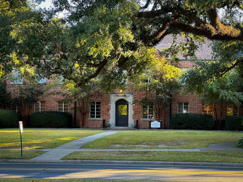 A large brick house with a black door is surrounded by trees and bushes.