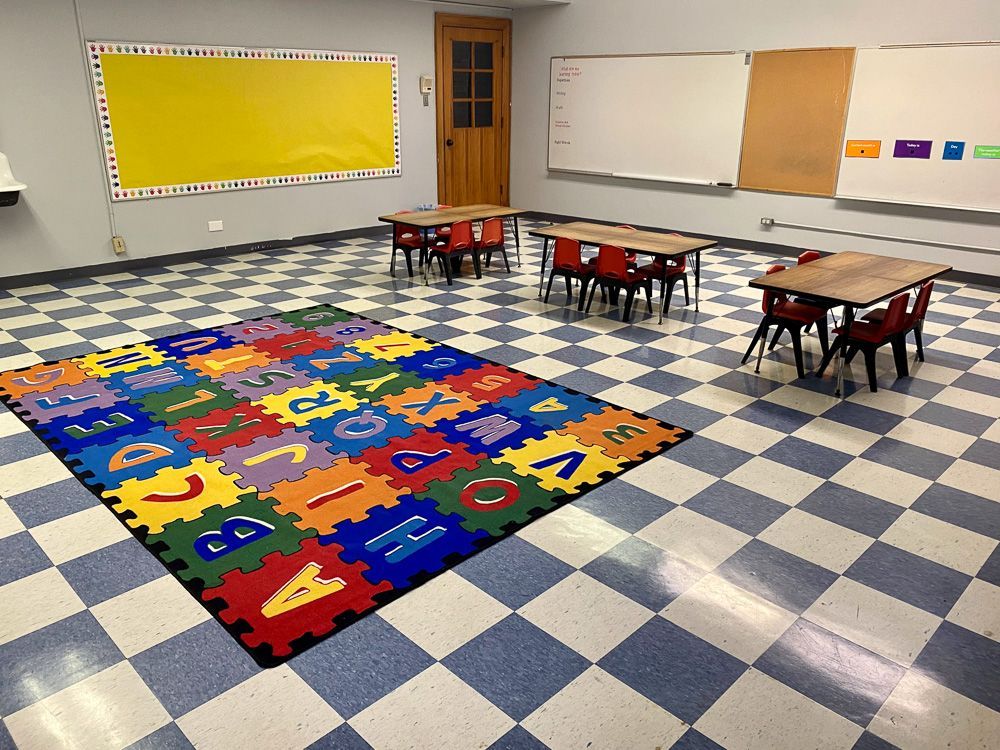 A classroom with tables and chairs and a rug with numbers on it