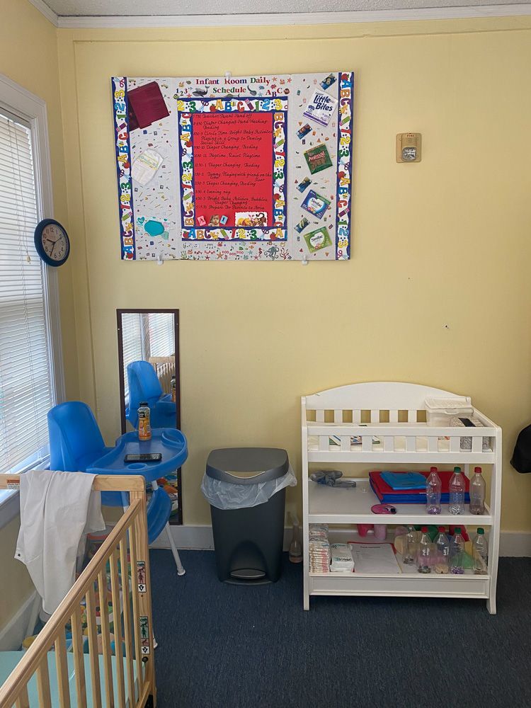 A baby room with a crib , high chair , changing table , mirror and a sign on the wall.