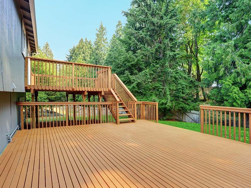 A large wooden deck with stairs leading up to it is in the backyard of a house.