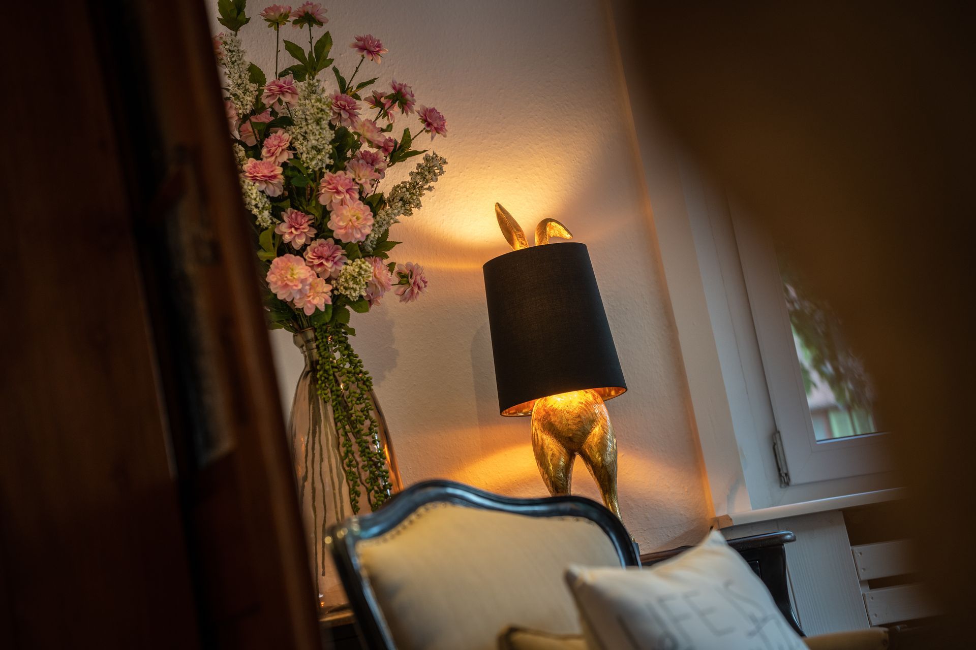 A lamp is sitting next to a chair in a room with a vase of flowers on the wall.