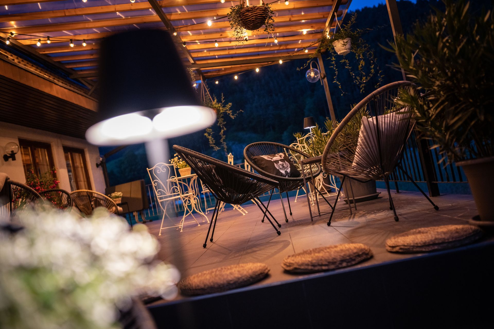 A patio with chairs , tables and a lamp at night.