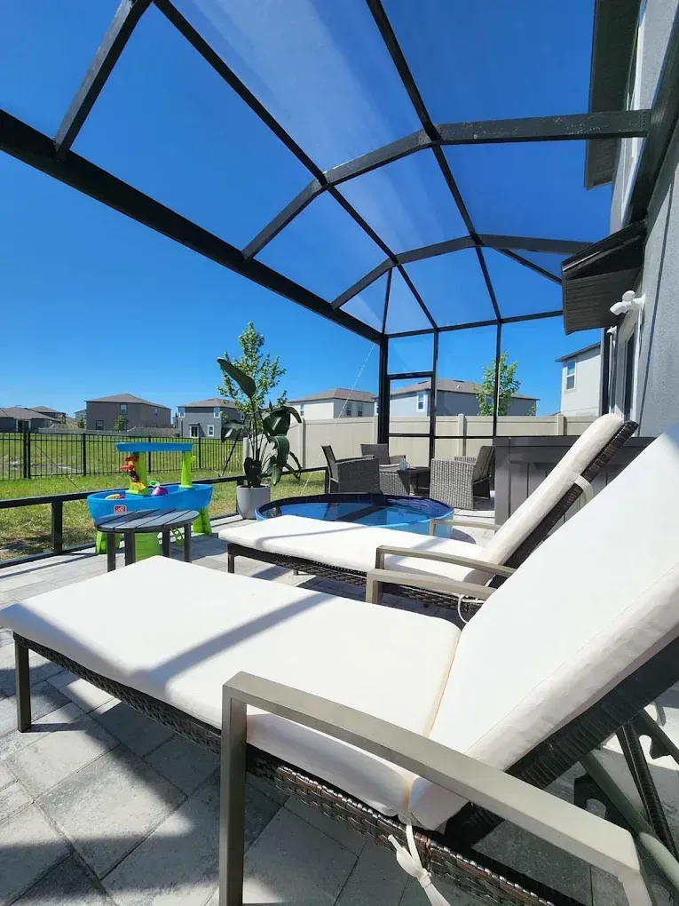 Patio with lounge chairs, pool under screened enclosure, clear blue sky.