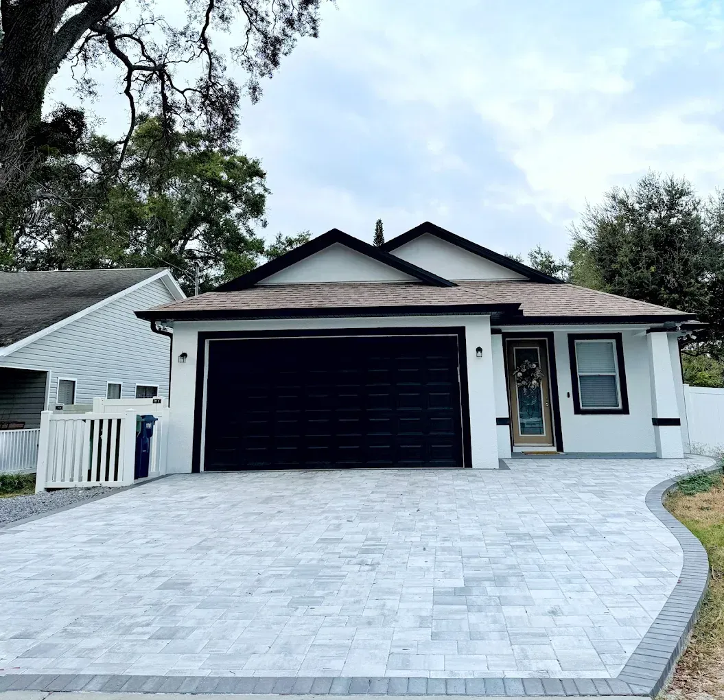 A modern, white house with a black garage door and paved driveway.