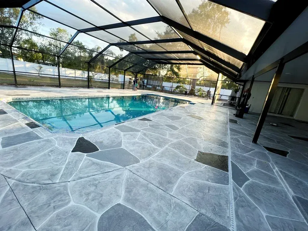 Pool with a blue interior, enclosed by a screened roof and decorated flagstone style concrete.