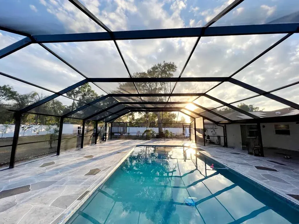 Pool covered by a black screened enclosure with the sun shining through.