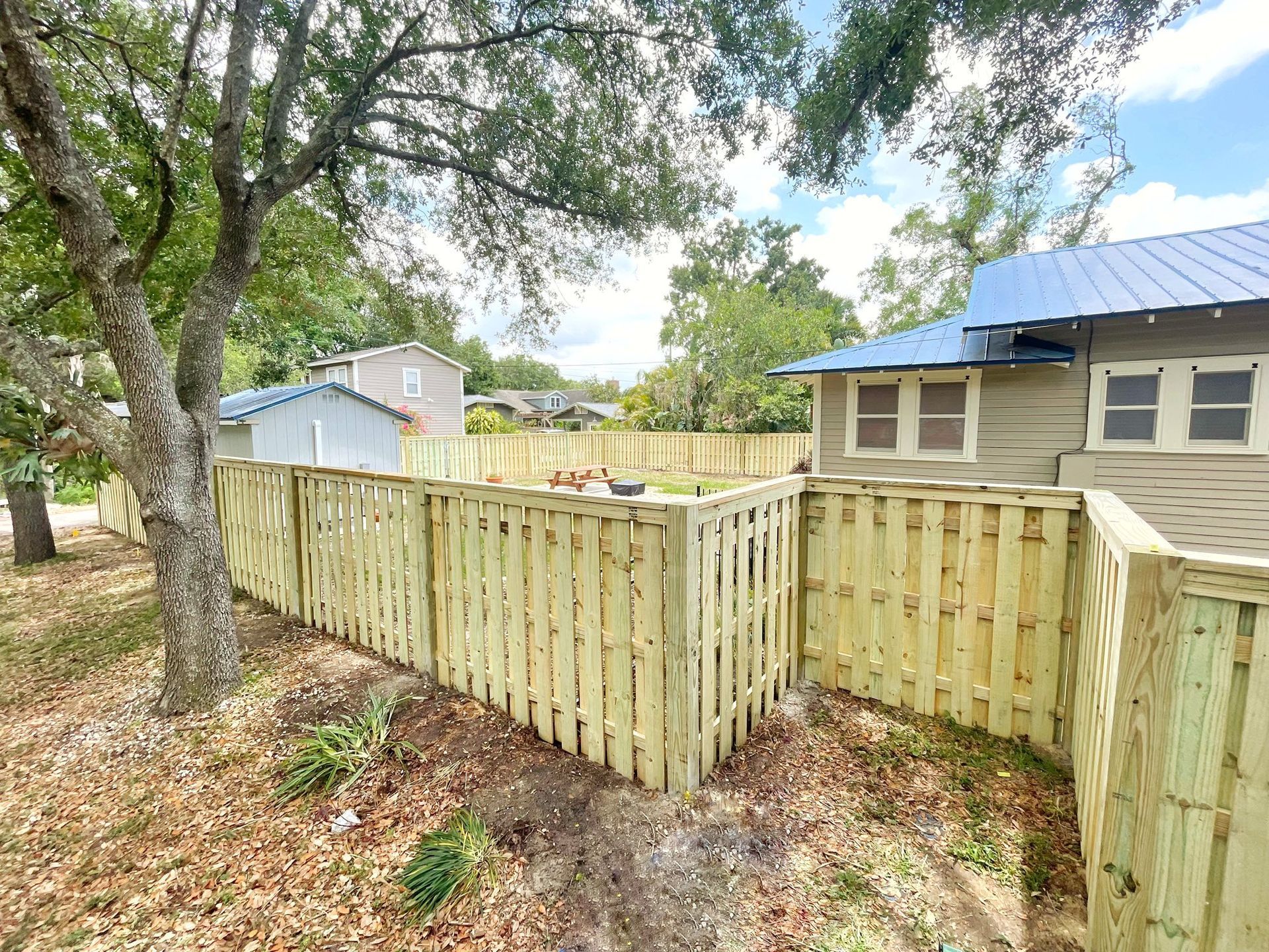 Wooden fence around a yard; a house with a blue roof is visible in the background.