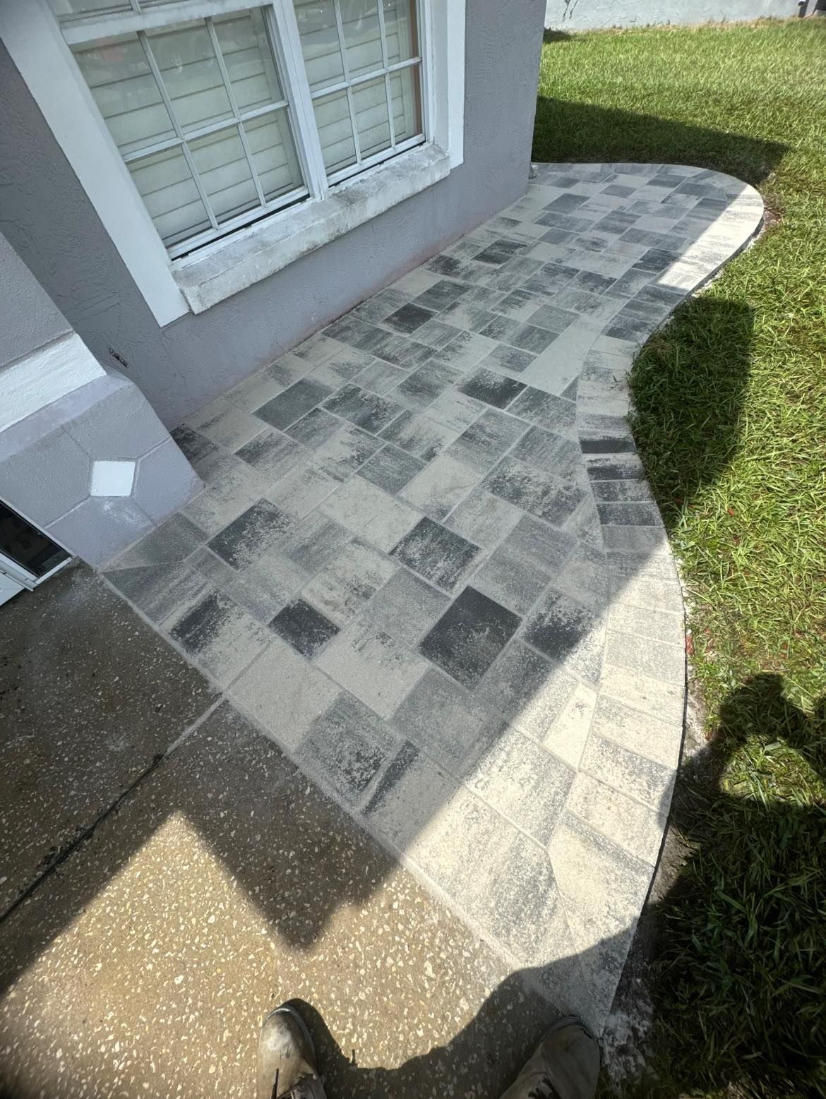 Paved walkway made of gray and light tiles leading to a building with a white window.