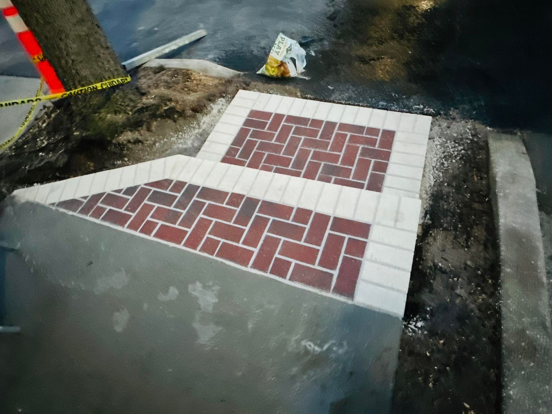 Concrete steps with brick-patterned inlays, near a tree, construction site, red and beige bricks.