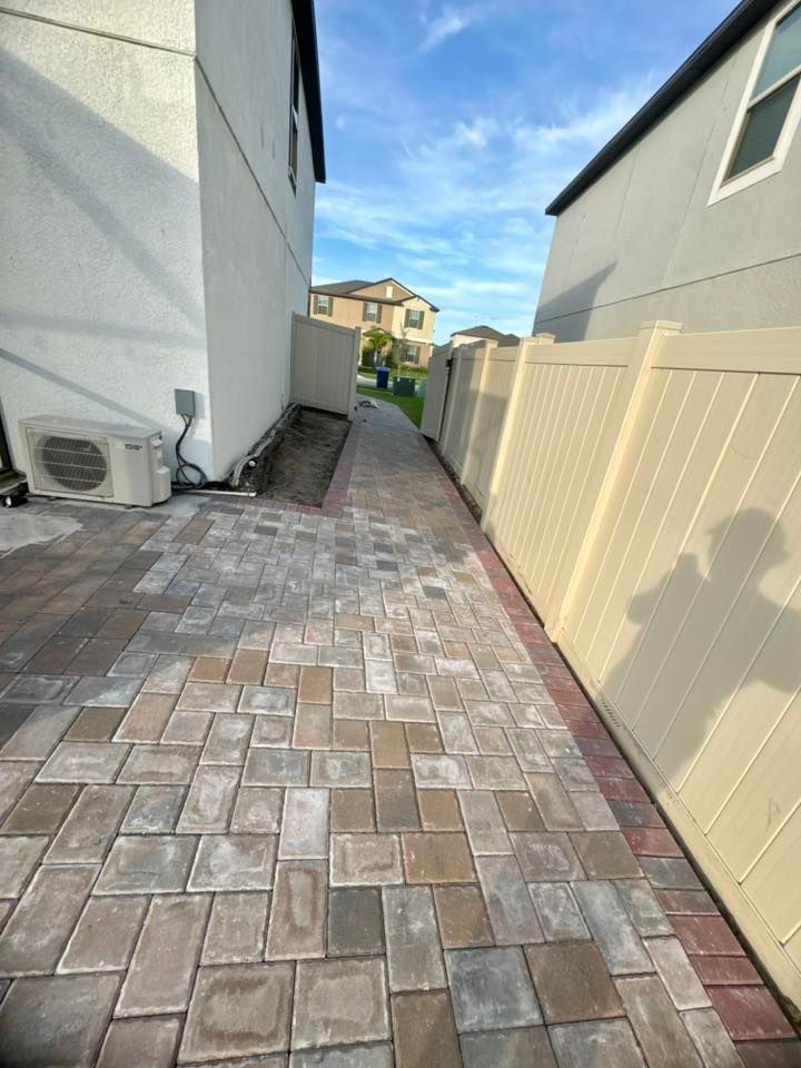 Brick paved walkway between two buildings and a fence, under a blue sky.