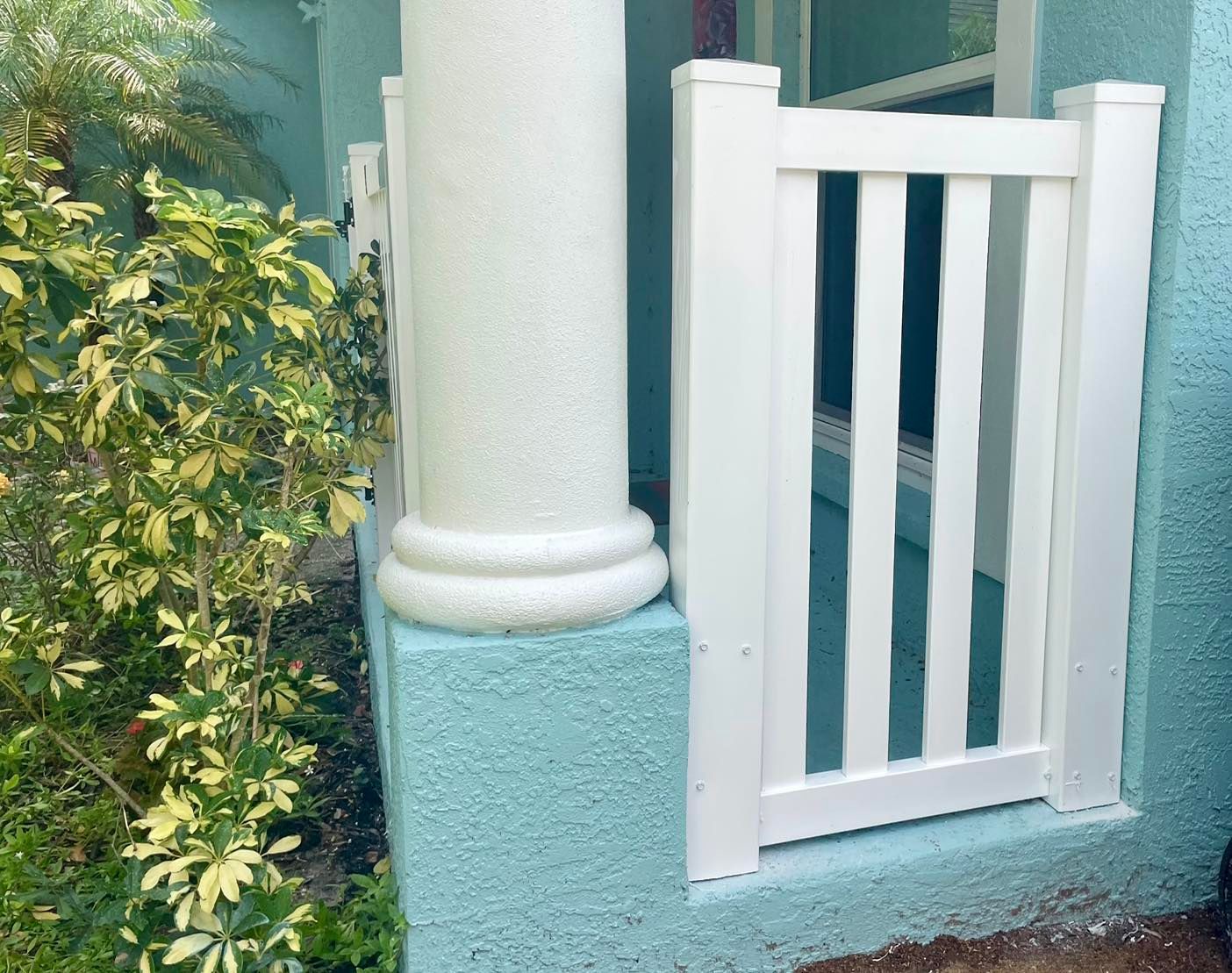 White picket gate next to a white column and teal wall; plants in the foreground.