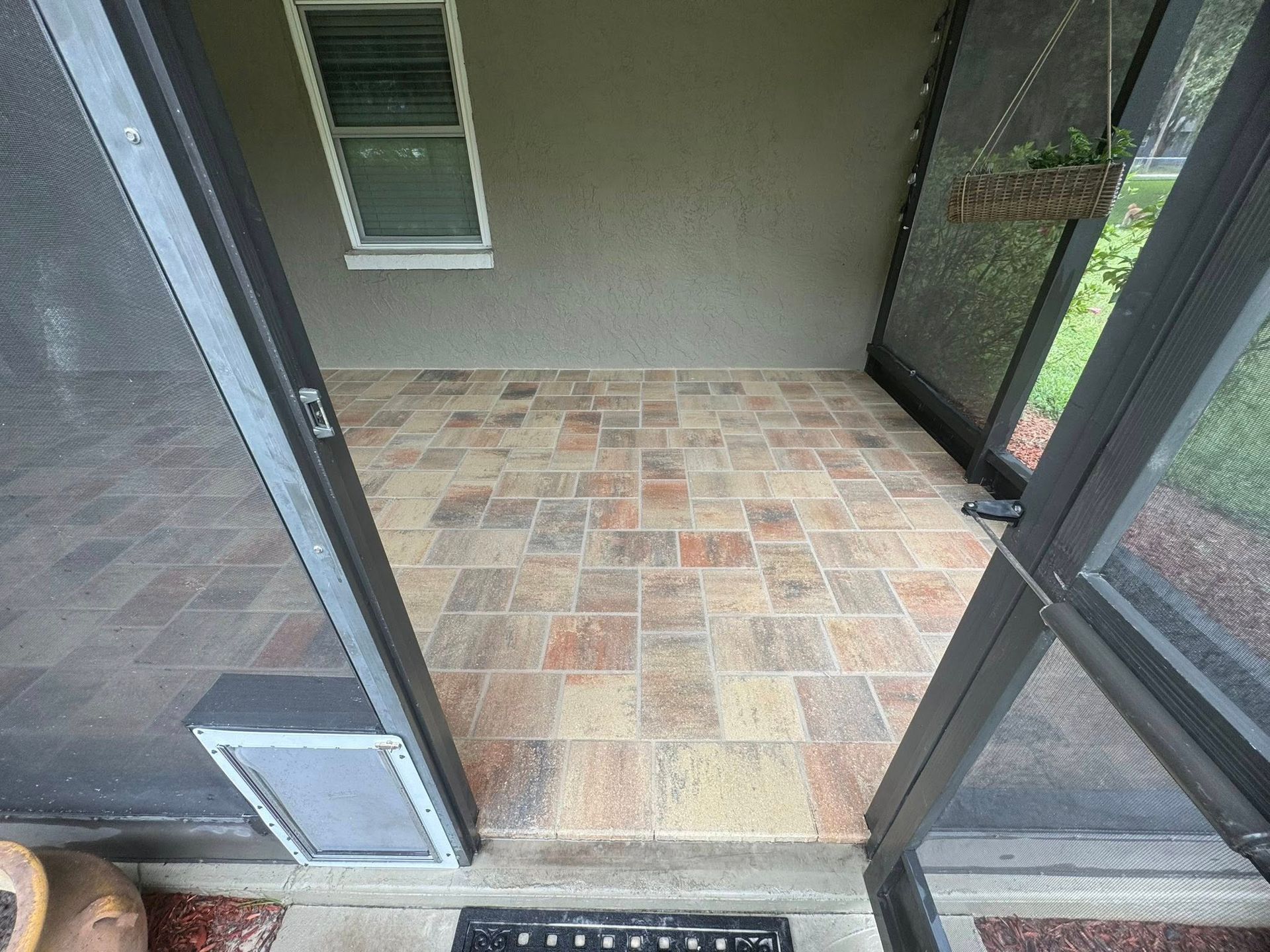 Screened patio with brick pavers, window, and hanging plant. Two screen doors open.