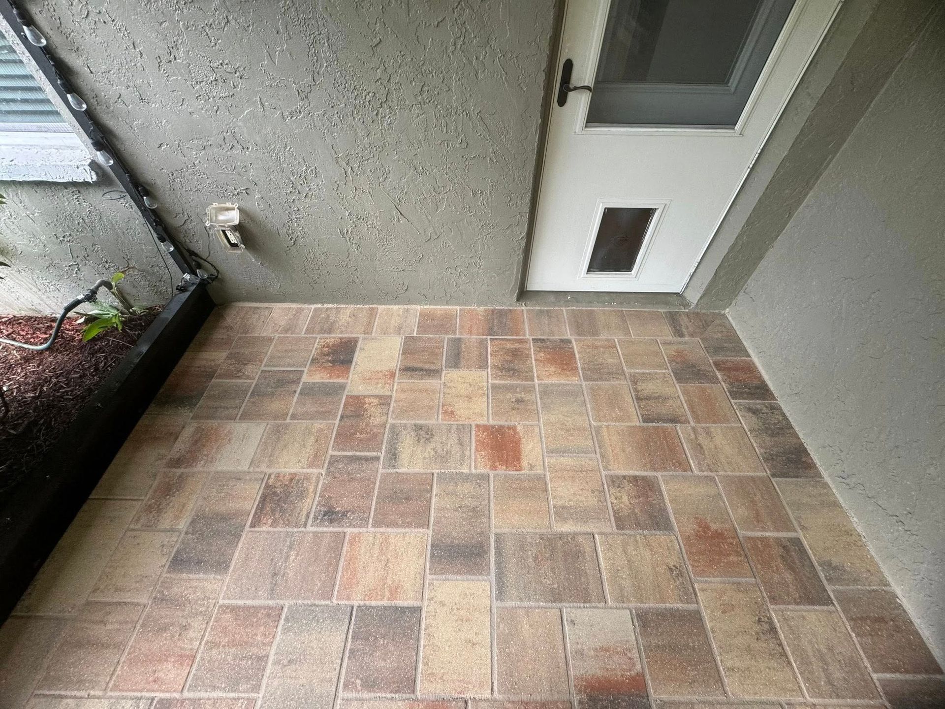 Tiled patio with a doorway, featuring a textured beige and brown brick pattern.