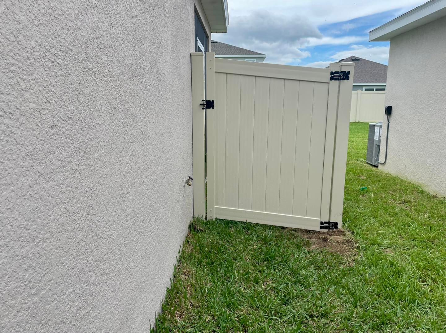 Beige gate in grassy yard next to a stucco wall.
