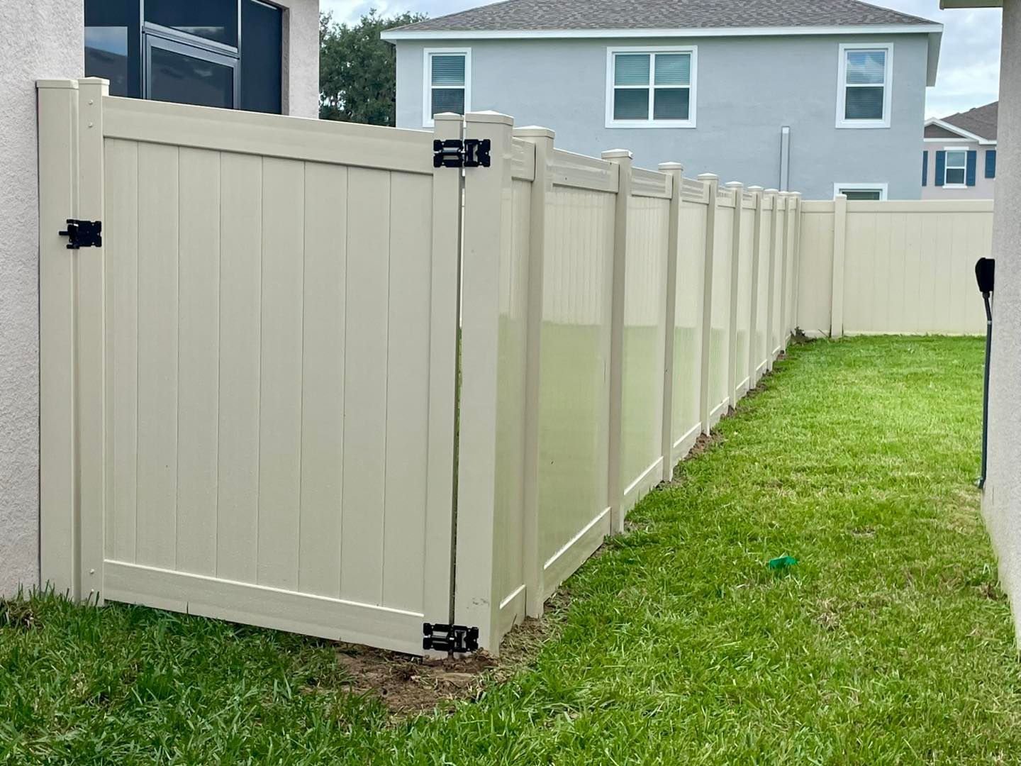 Tan vinyl fence with a gate in a grassy yard near a house.