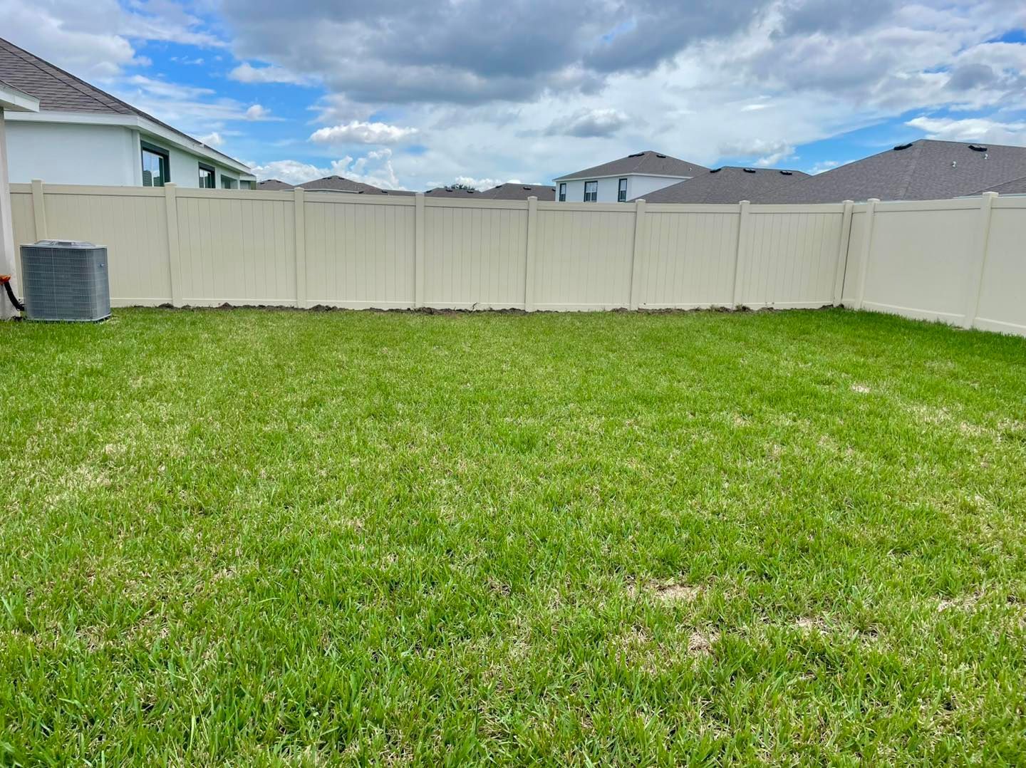 Backyard with green grass, beige fence, and overcast sky.