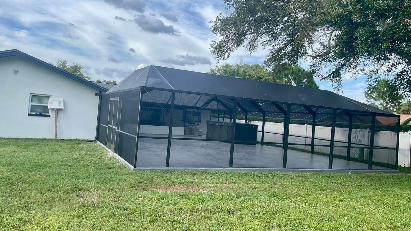 Screened-in patio with dark frame, concrete floor, and a portion of a white house.