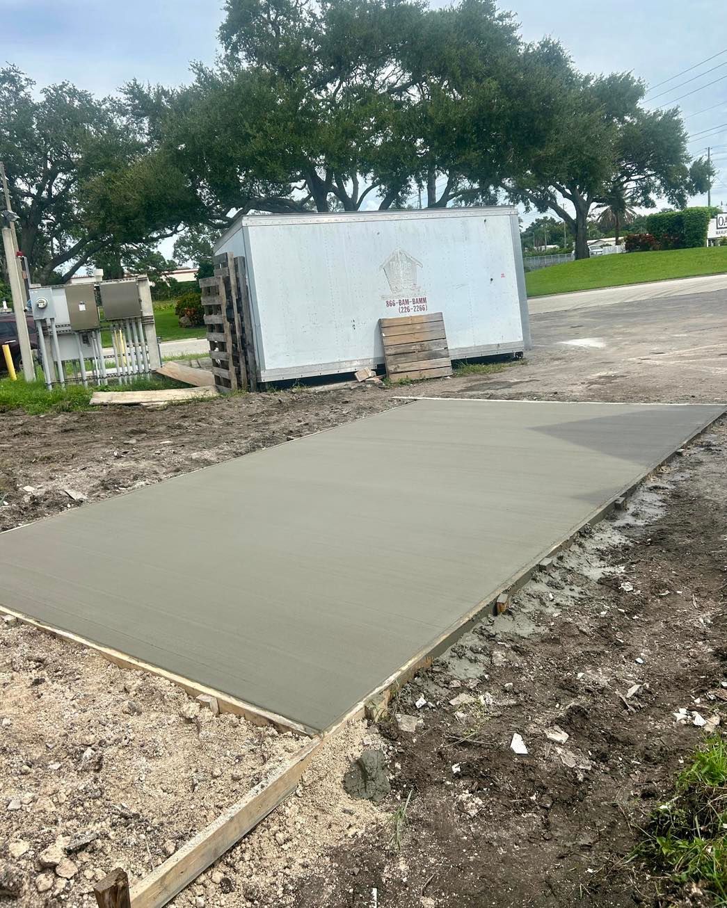 Freshly poured concrete slab in a construction zone. Brown framing and ground, trees in the background.