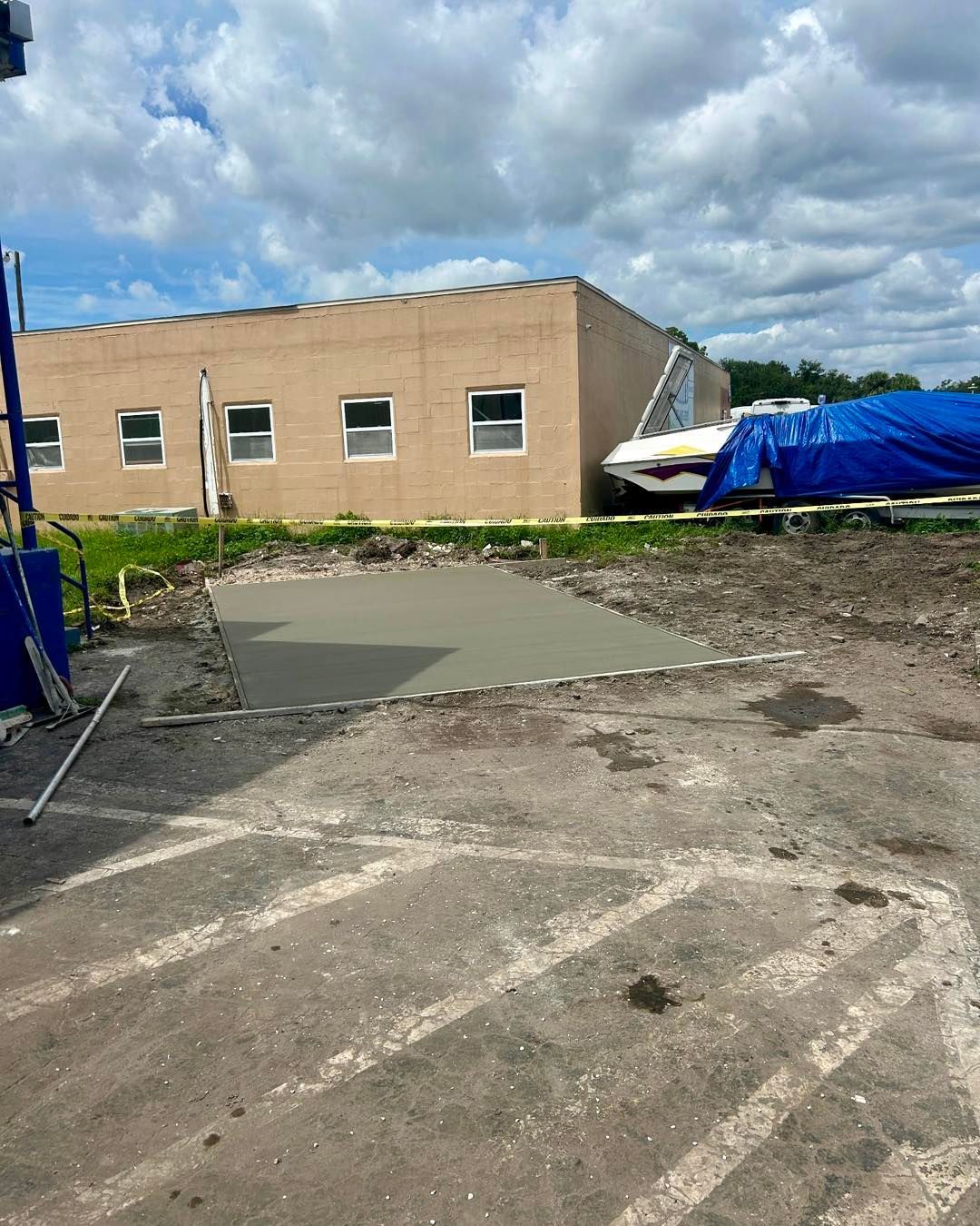 Freshly poured concrete pad in an outdoor area, with a building and a boat in the background.