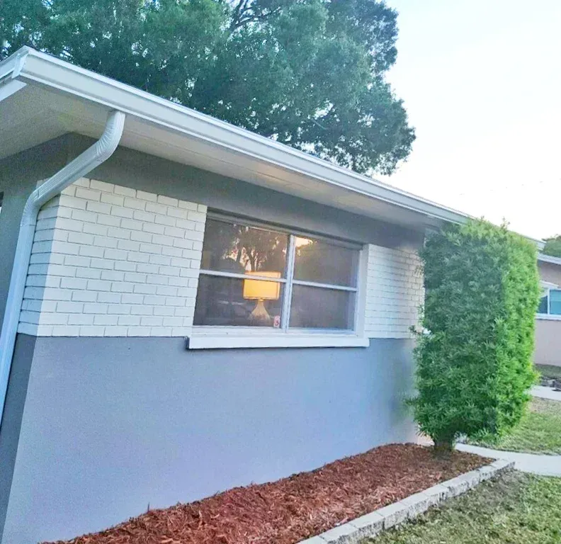 Exterior of a house with light gray brick and dark gray lower section, window, tree, and mulch.
