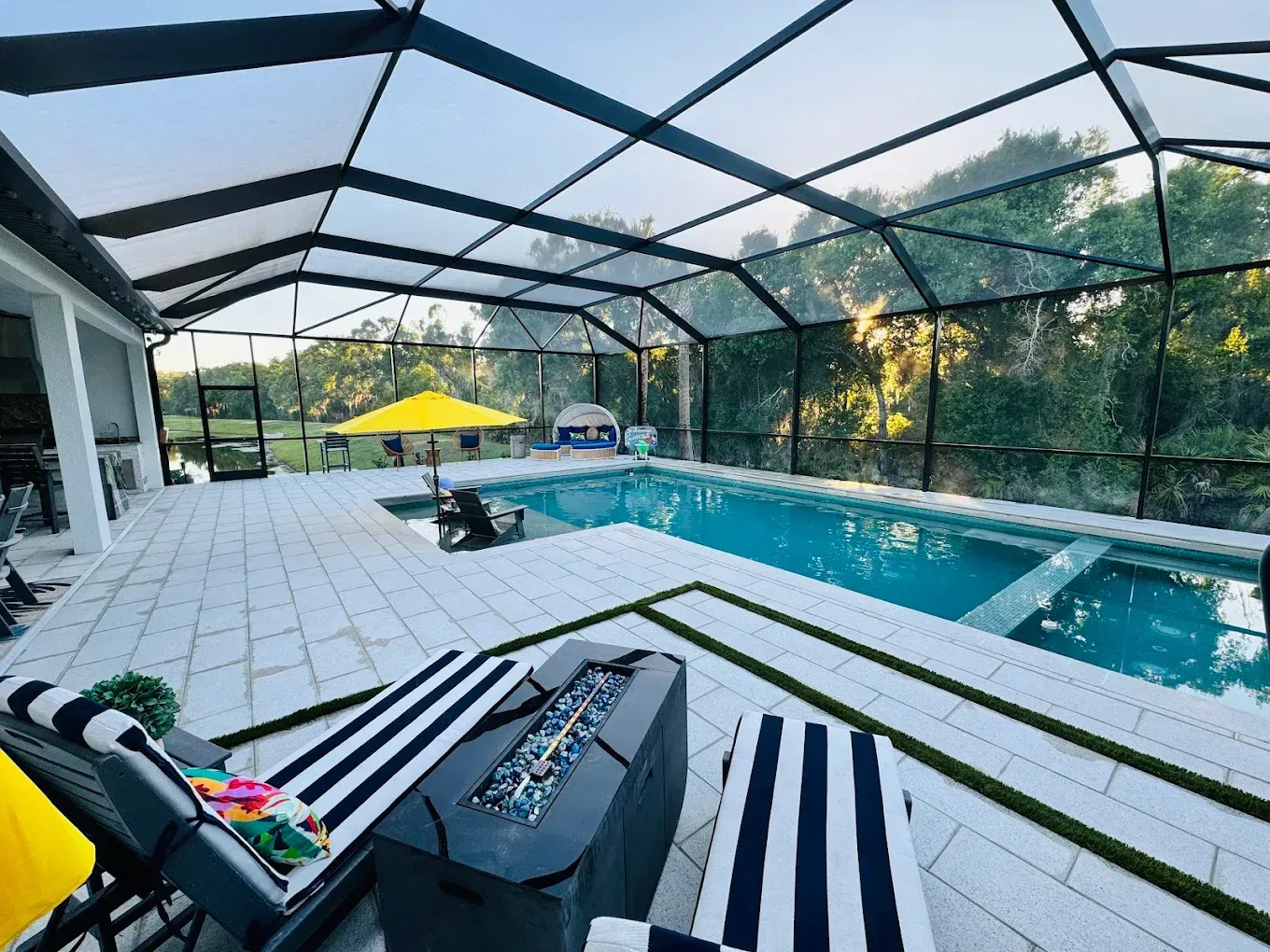 Pool area with screened enclosure, pool, patio furniture, and a fire pit.