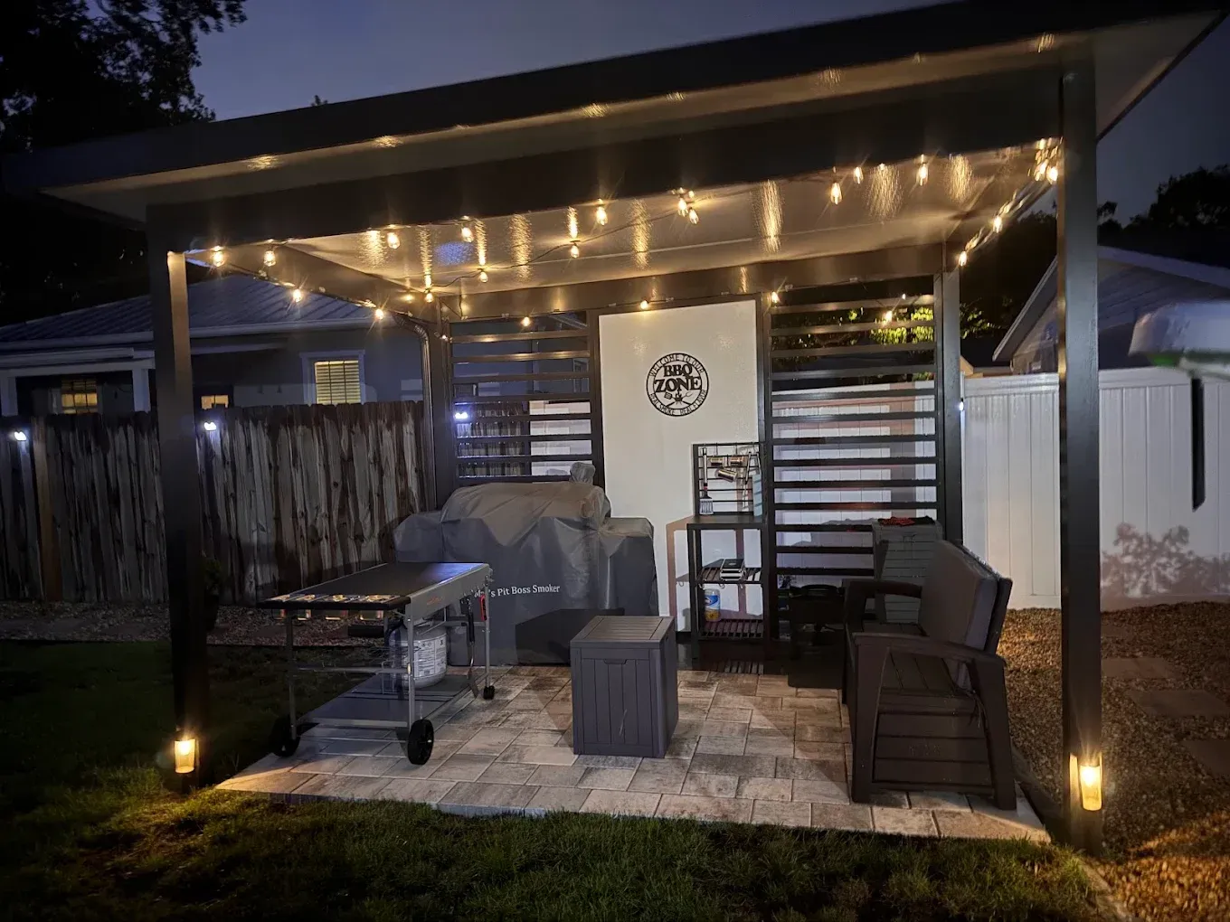 Patio at night with string lights, grill, seating, and a decorative wall.