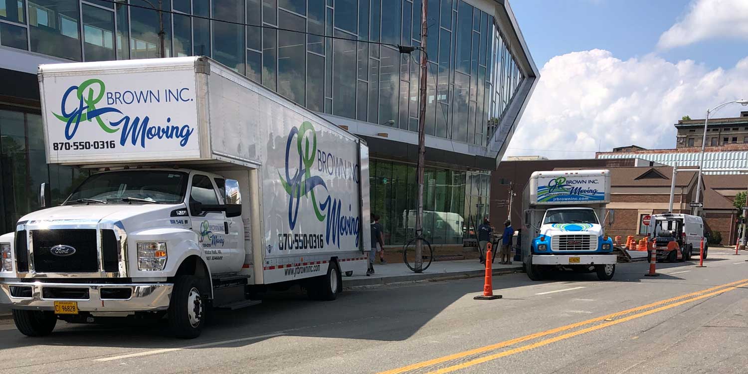 Two moving trucks are parked on the side of the road in front of a building.