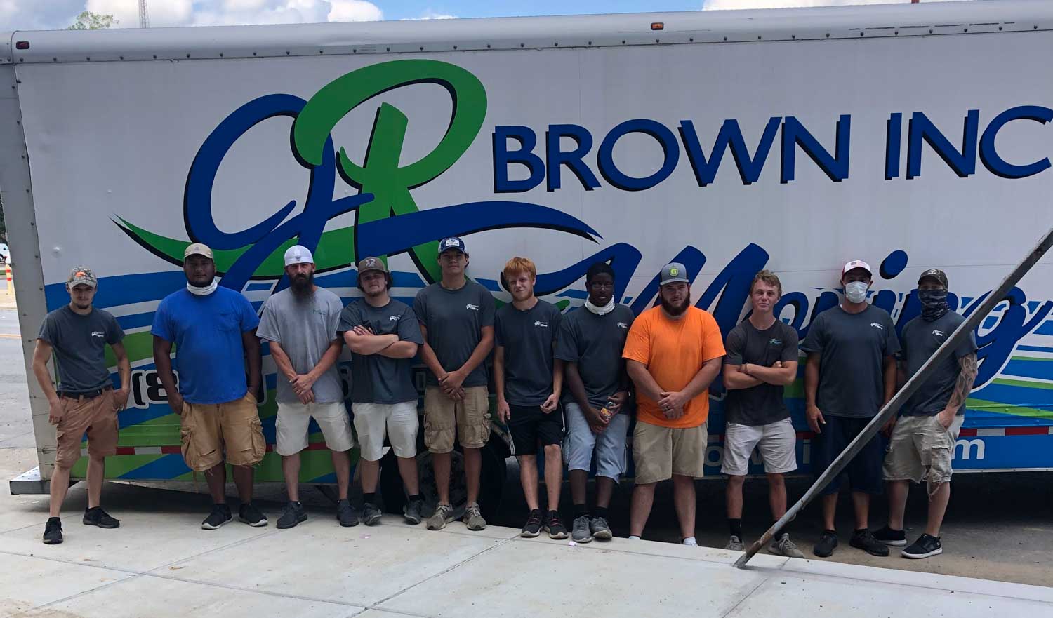 A group of men are posing for a picture in front of a brown inc. truck.