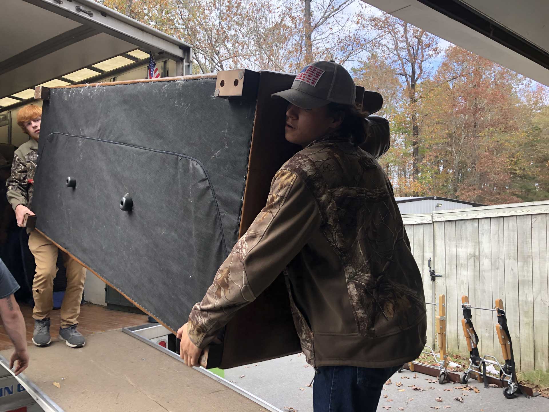 A man in a hat is carrying a large piece of furniture.