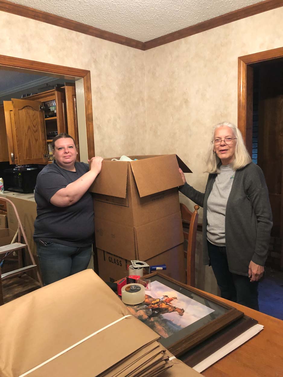 Two women are standing next to each other in a room holding a cardboard box.