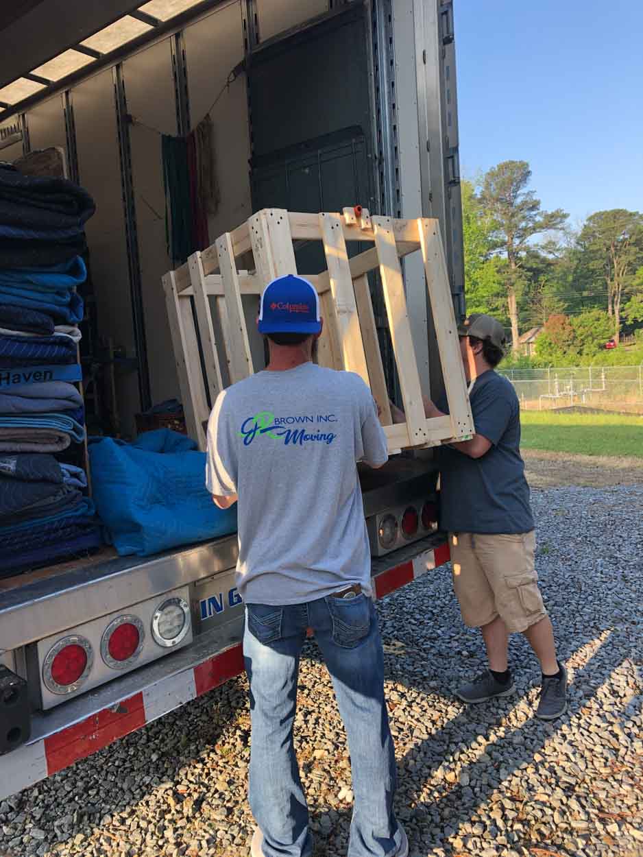 Two men are carrying a wooden crate out of a truck.