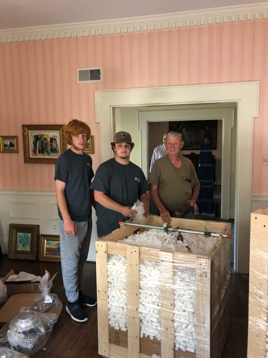 Two men are standing next to a wooden crate in a living room.