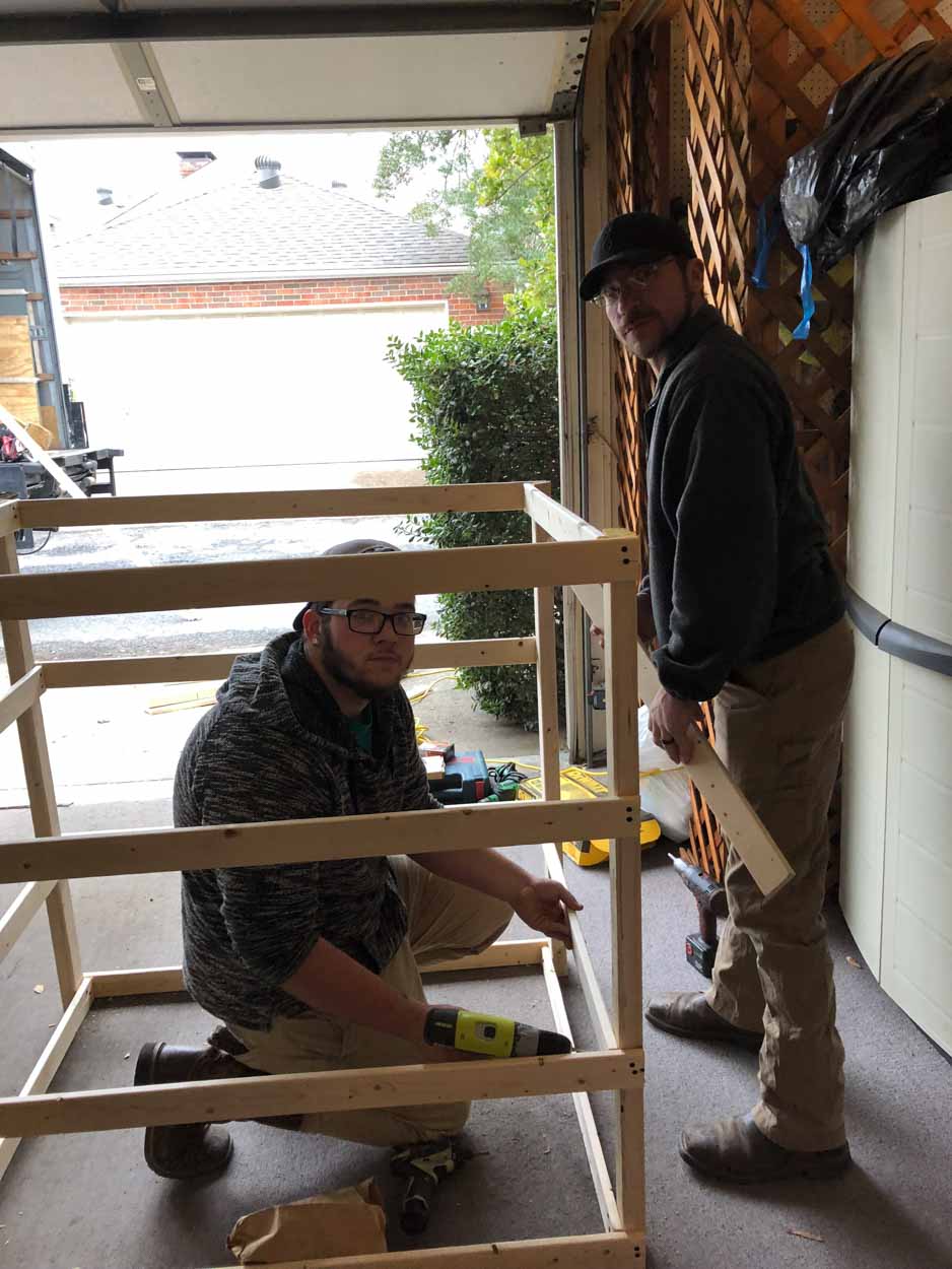 Two men are working on a wooden structure in a garage.