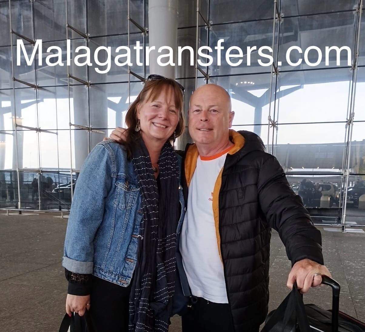 A man and a woman are posing for a picture in front of malagatransfers.com