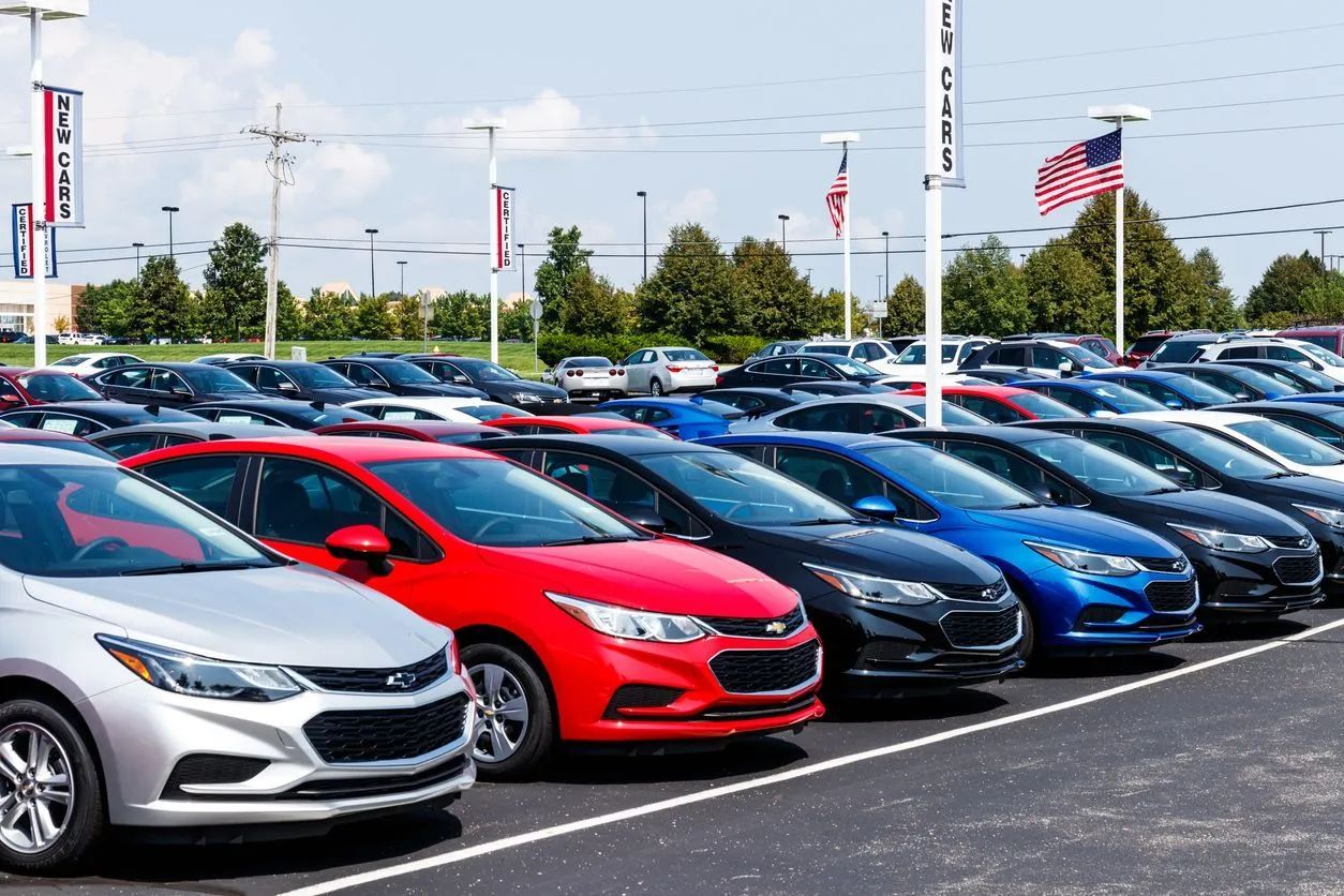 A row of various colored Chevrolet Cruze sedans parked in a dealership lot under a bright, sunny sky.