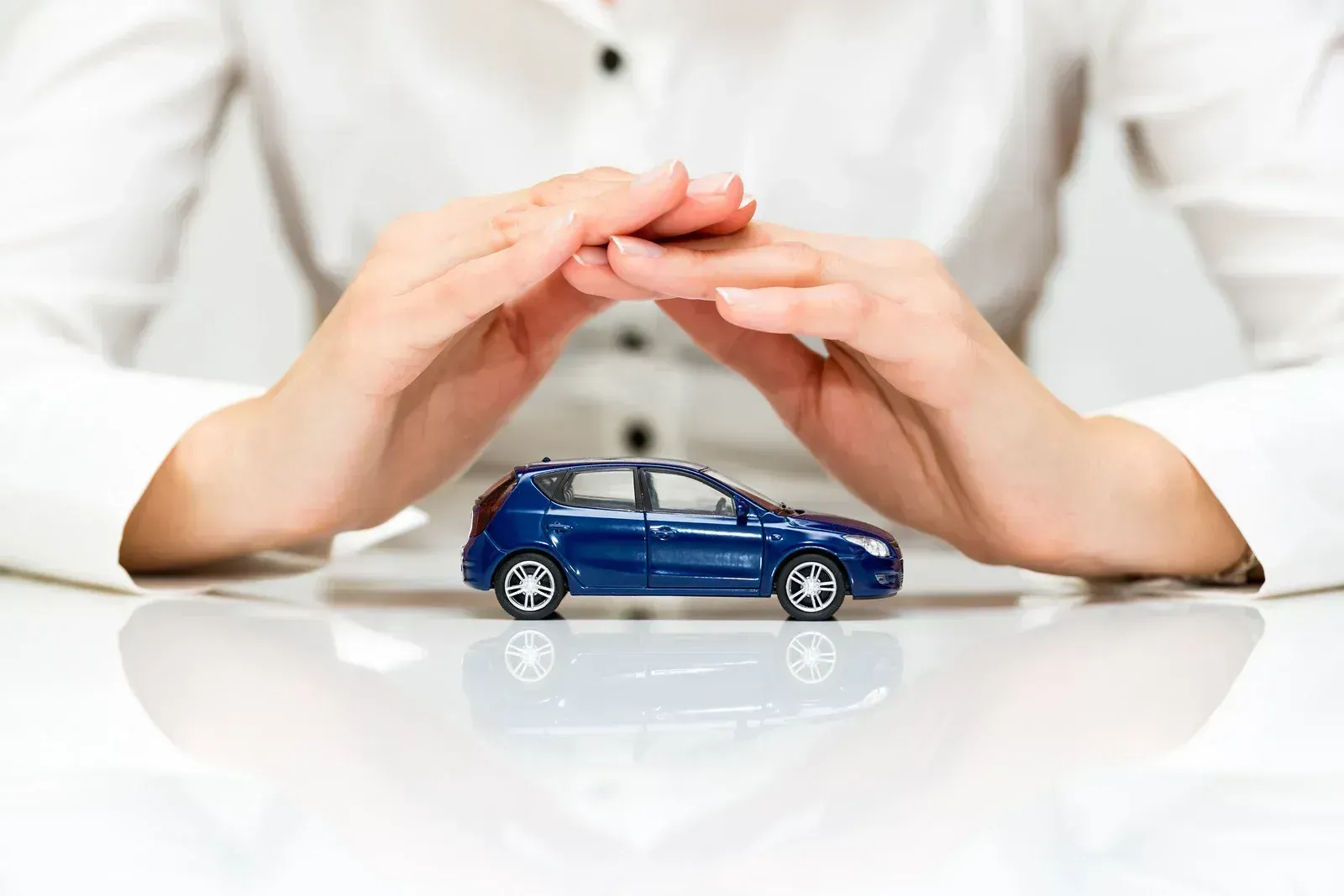 A woman is covering a toy car with her hands.