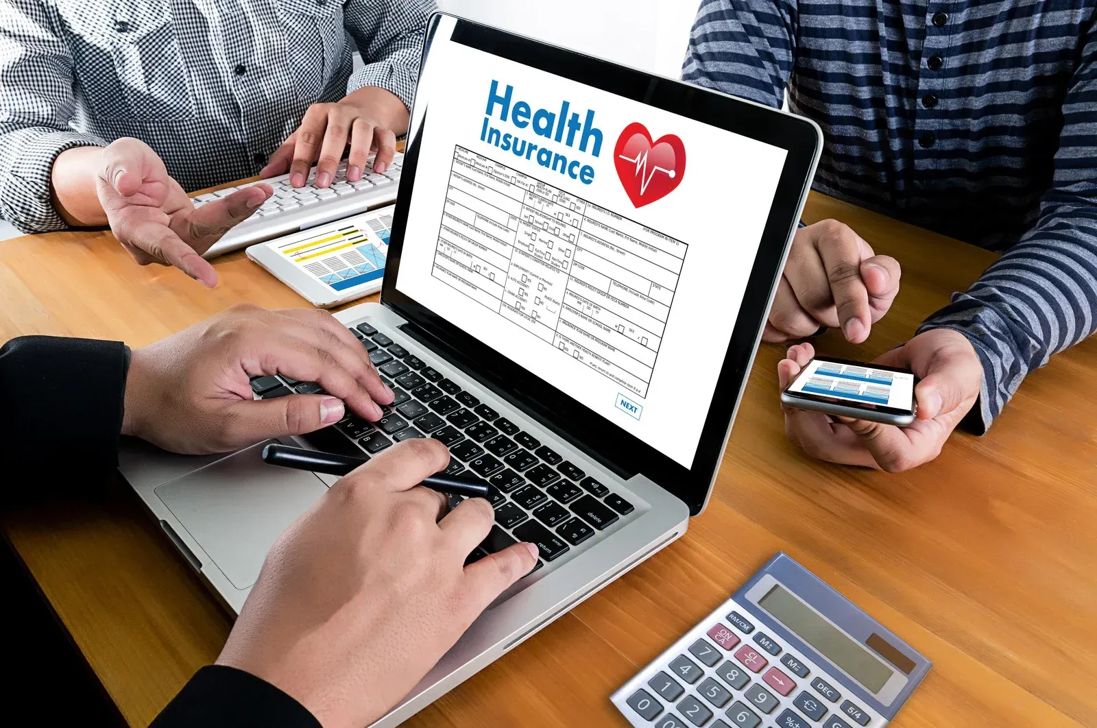 A person is typing on a laptop with a health insurance form on the screen.