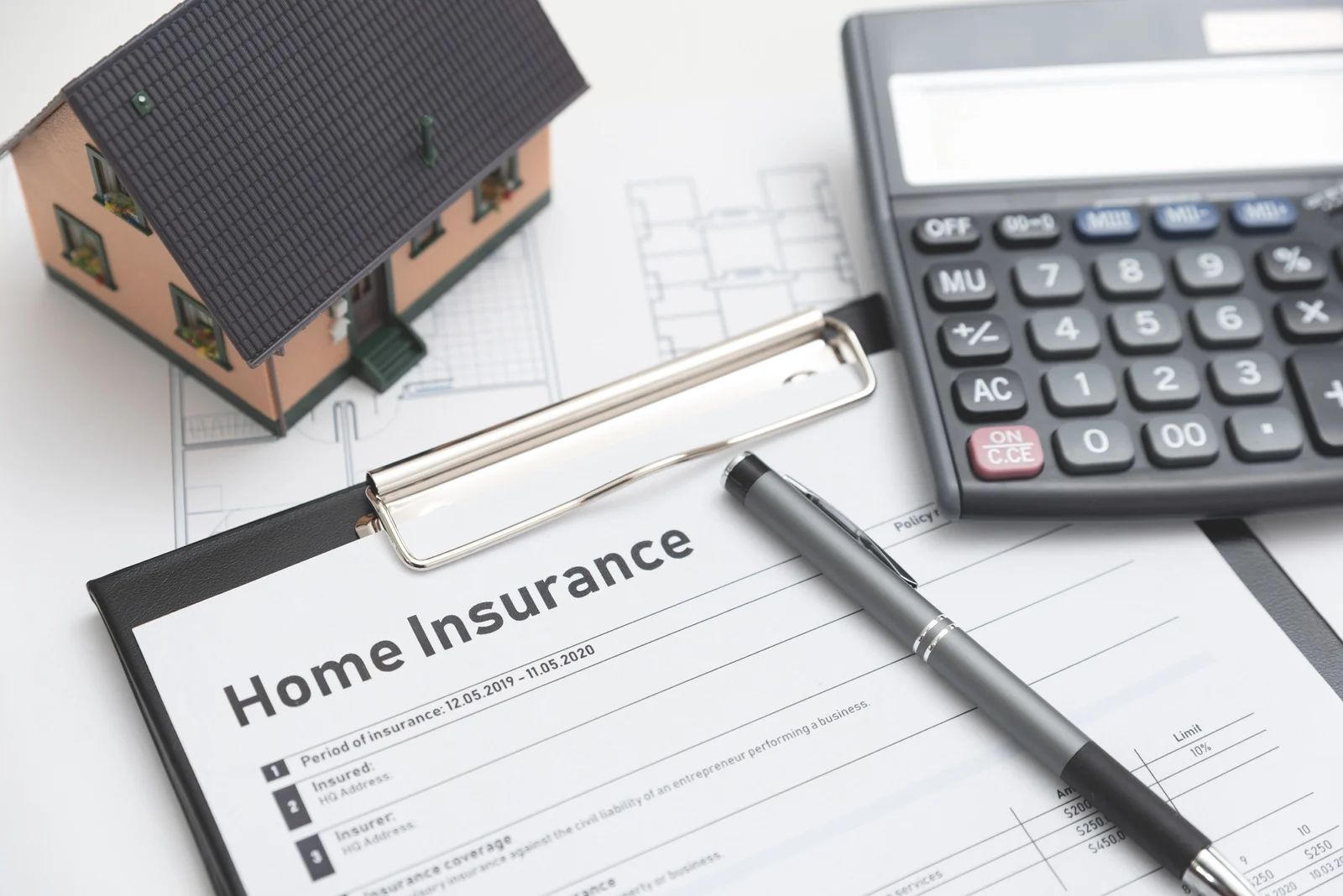 Home insurance form with model house, calculator, and pen on a desk.