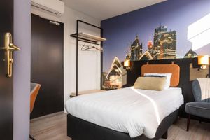 Een hotelkamer met een eenpersoonsbed en een foto van de skyline van een stad aan de muur.