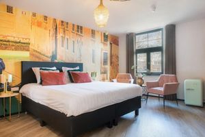 Een hotelkamer met een groot bed, stoelen en een schilderij aan de muur.