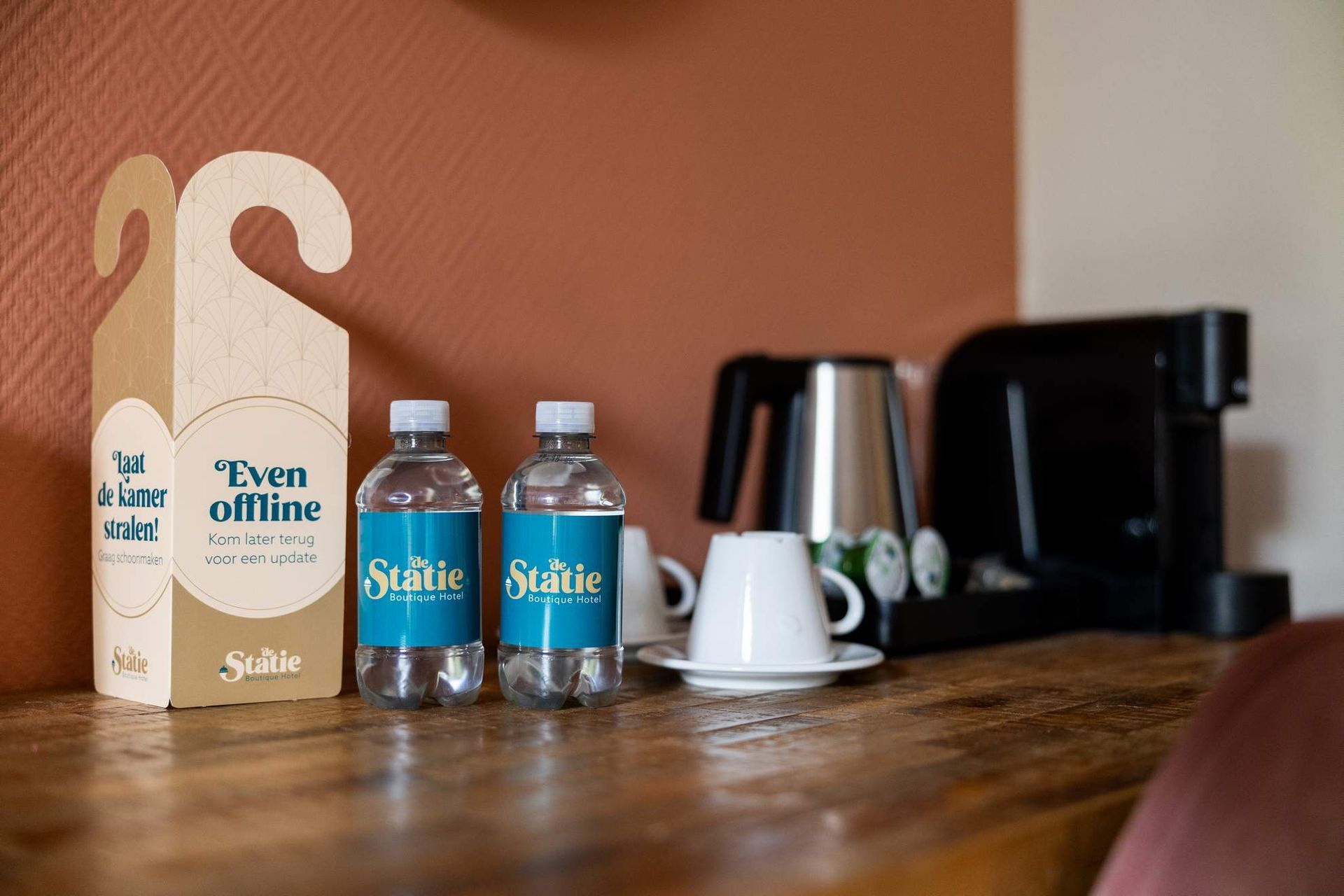 Houten tafel met waterflessen, kopjes, koffiezetapparaat en een deurhanger met de tekst 