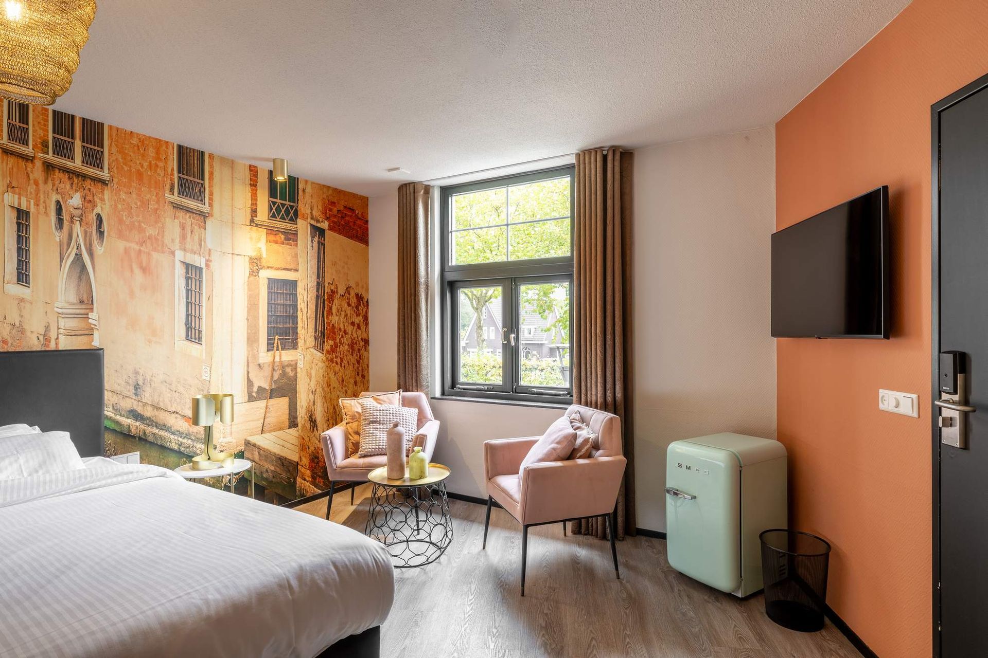 Een hotelkamer met een groot bed, stoelen en een schilderij aan de muur.