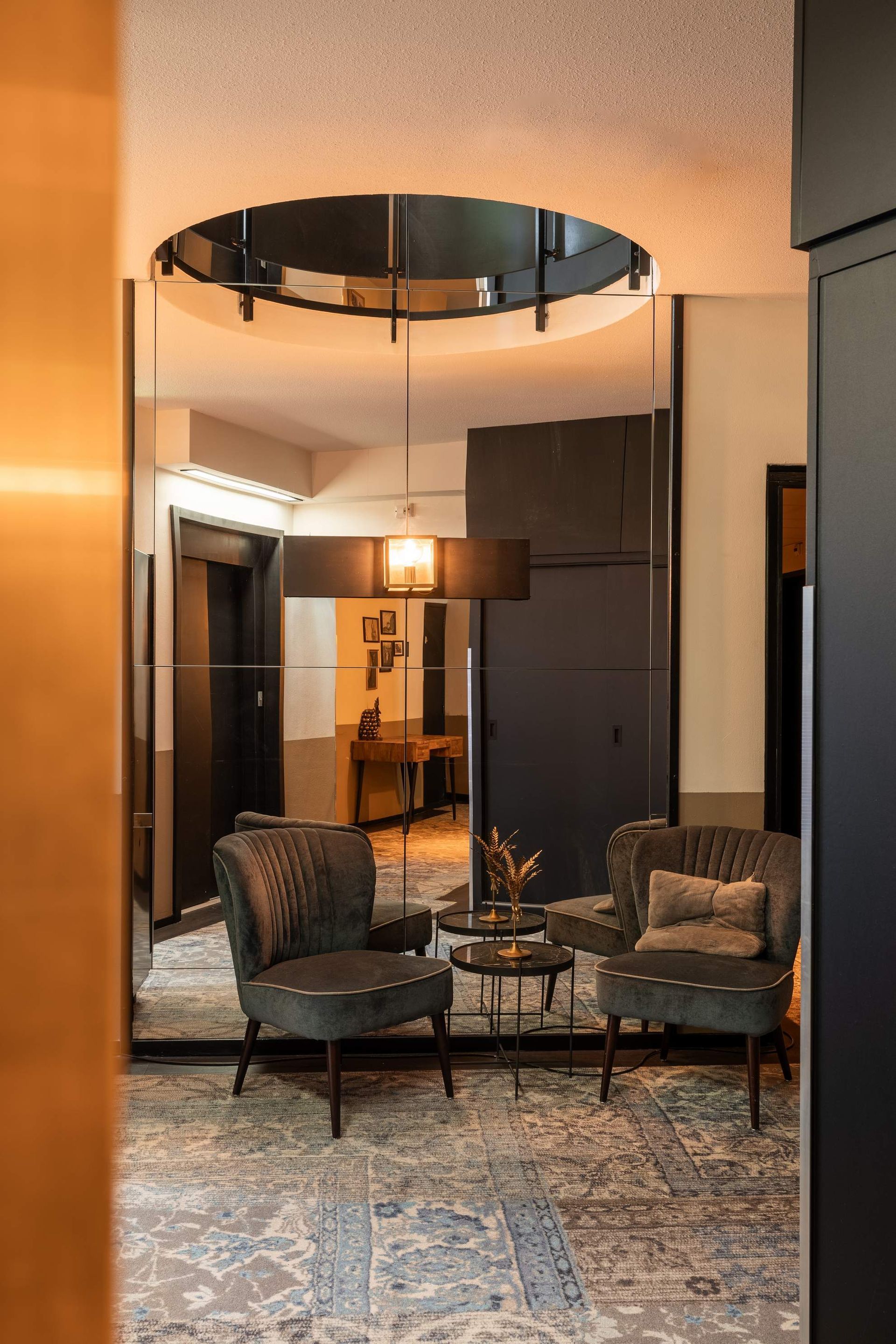 Twee groene fluwelen fauteuils in een kamer met een grote spiegel, een tapijt en een klein rond tafeltje.