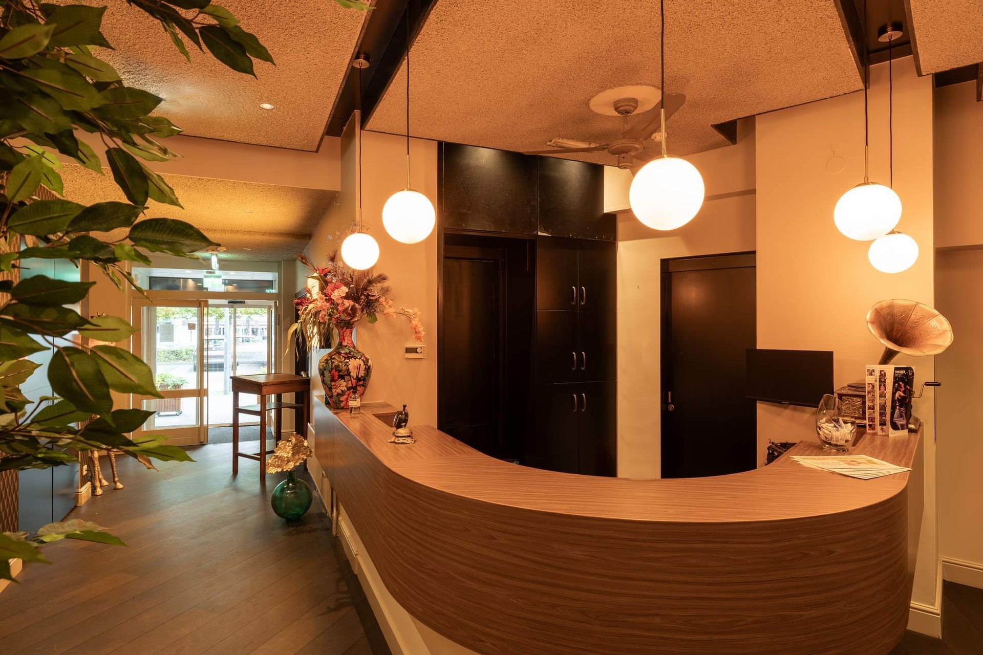 Receptie in de hotellobby met hanglampen, bloemen en liftdeuren.