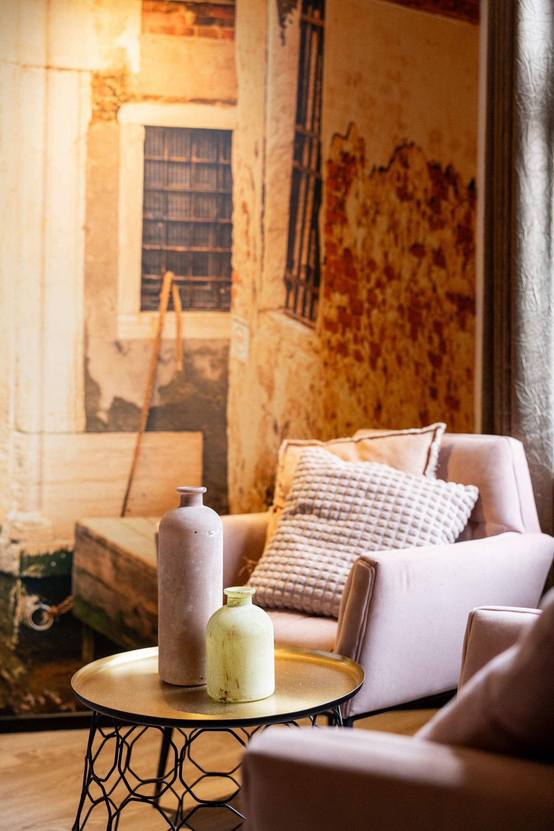 Leunstoel naast ronde tafel met vazen; muurschildering op de achtergrond van een kanaalscène in Venetië.