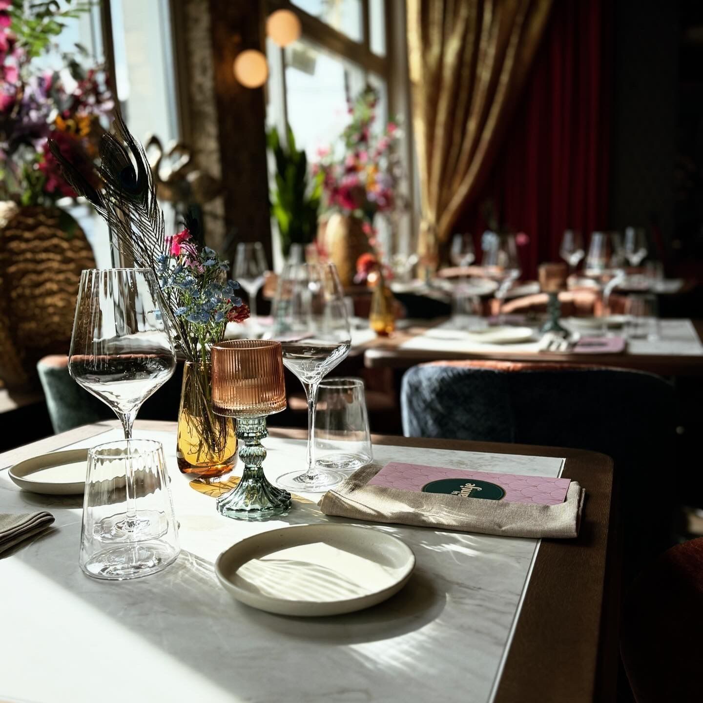 Elegante restauranttafel met glazen, bloemen en borden, badend in het zonlicht.