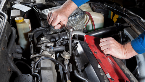 A man is working on the engine of a car with a wrench.