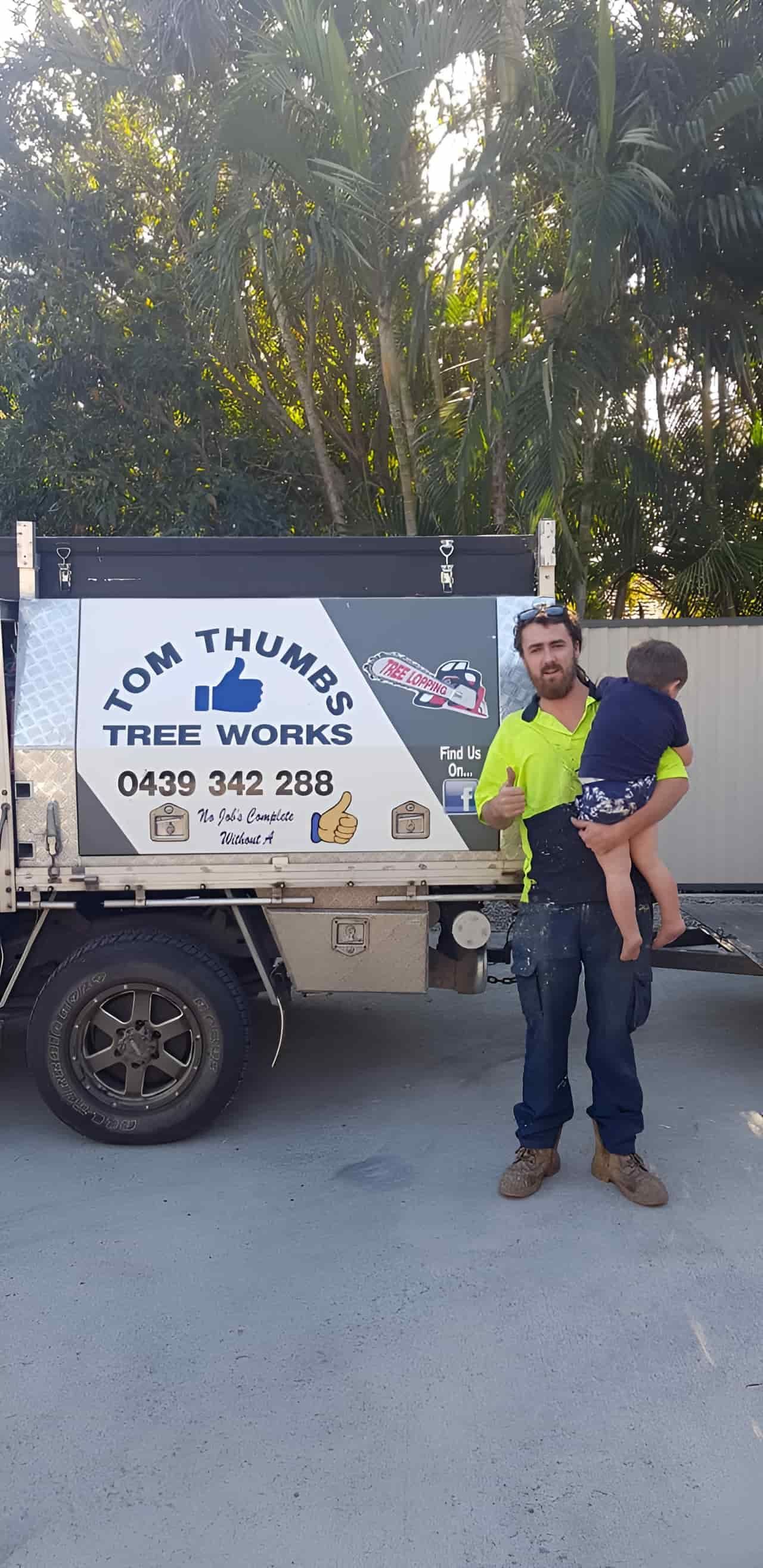 A Man Is Holding A Child On His Shoulders In Front Of A Truck — Tom Thumbs Tree Works In Bellmere, QLD