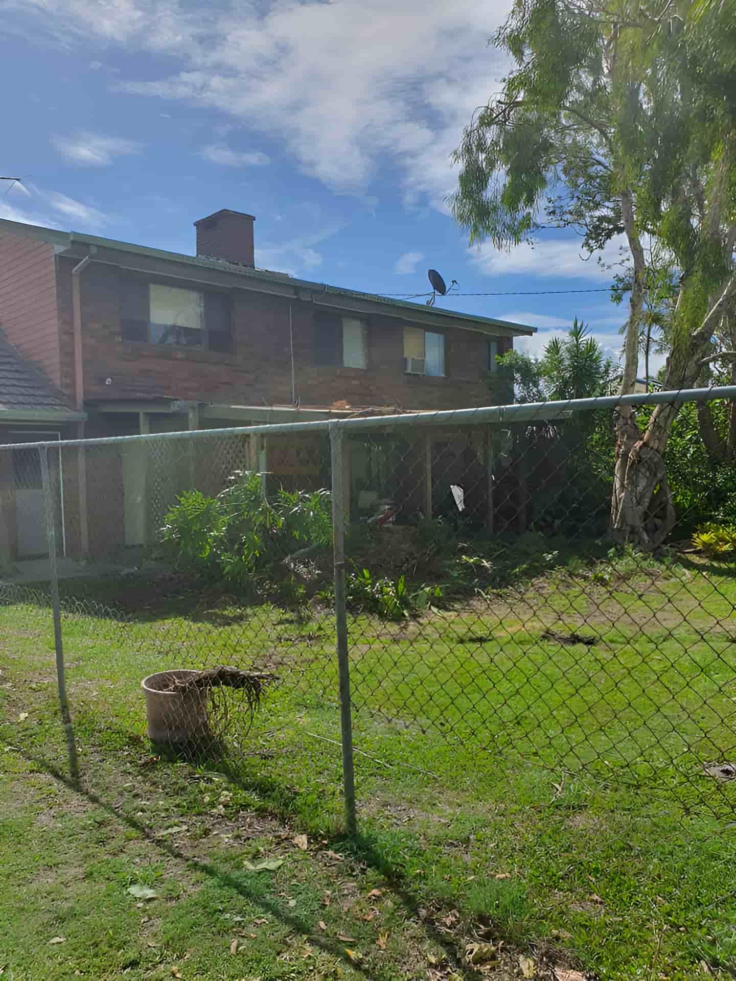 A Chain Link Fence Surrounds A Lush Green Yard In Front Of A Brick House — Tom Thumbs Tree Works In Deception Bay, QLD